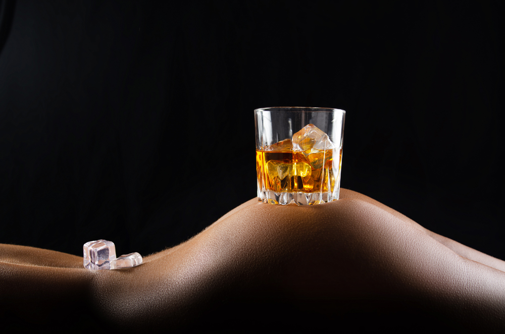 Caucasian laying down model holds glass of whiskey with icecubes